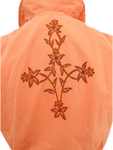 Close-up of the back of a peach-colored garment featuring a large embroidered floral vine design in a contrasting reddish-brown thread.