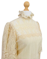 A cream-colored vintage lace blouse displayed on a wooden dress form mannequin, featuring a high ruffled collar and long lace sleeves.