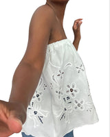 White strapless top with floral patterns worn by a person, with a blurred background.