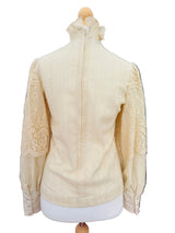 A cream-colored blouse with textured vertical stripes and lace sleeve panels, displayed on a dress form mannequin.