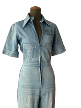 A light blue denim short-sleeve jumpsuit displayed on a black mannequin 